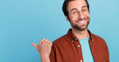 Photo of cute brunet young guy index promo wear spectacles trend fit isolated on blue color background.