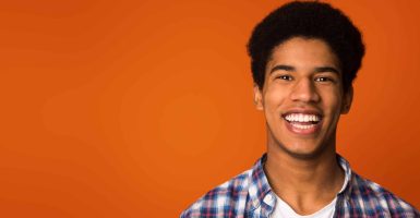 Portrait of happy student in checkered shirt looking at camera, orange background