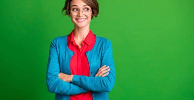 Photo of young cheerful girl happy smile positive dream dreamy crossed hands look empty space isolated over green color background.